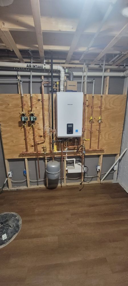 Plumbing installation on plywood with water heater, expansion tank, and copper pipes in a room.