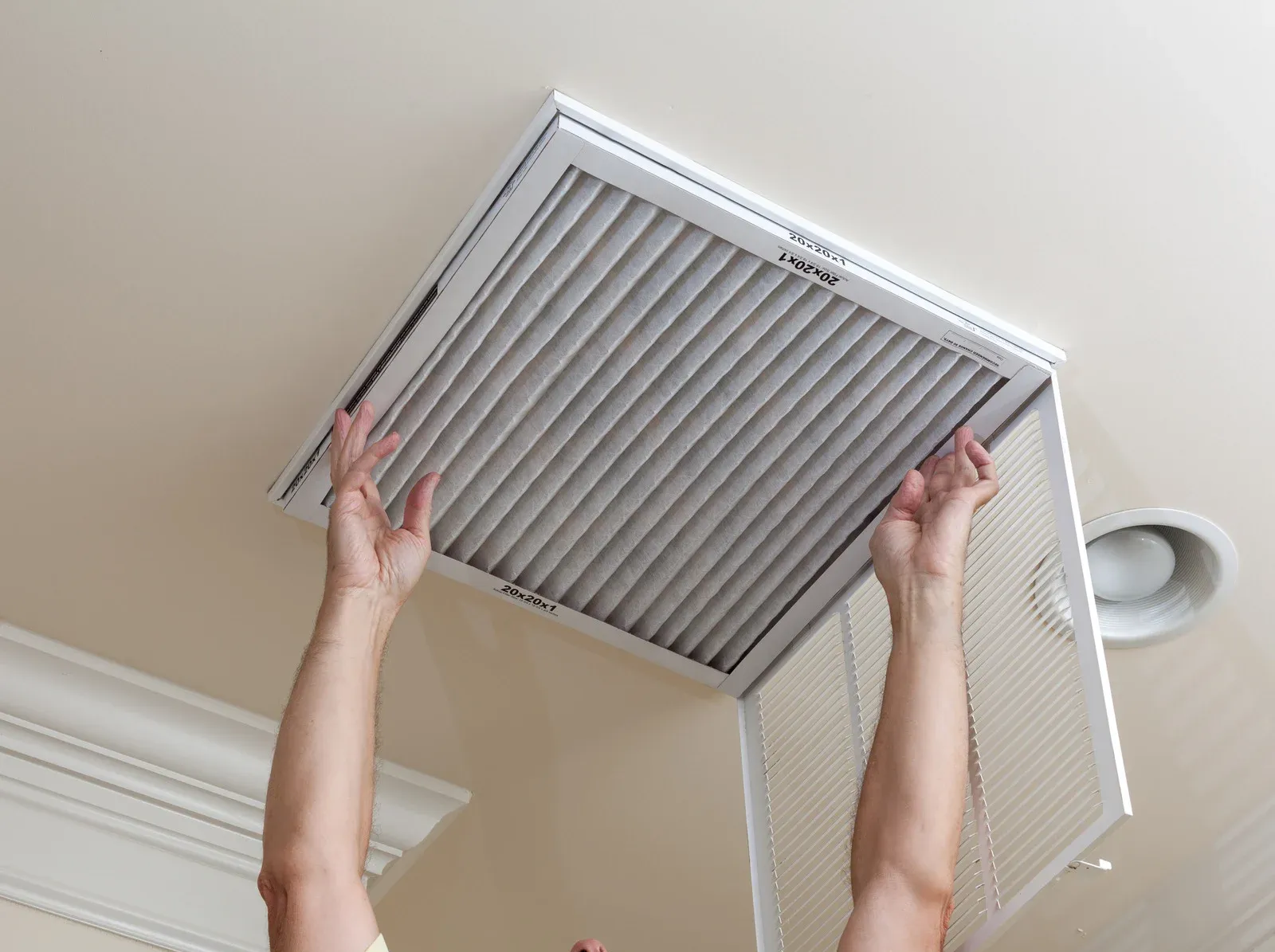 Person removing an air filter from a ceiling vent in a white room.