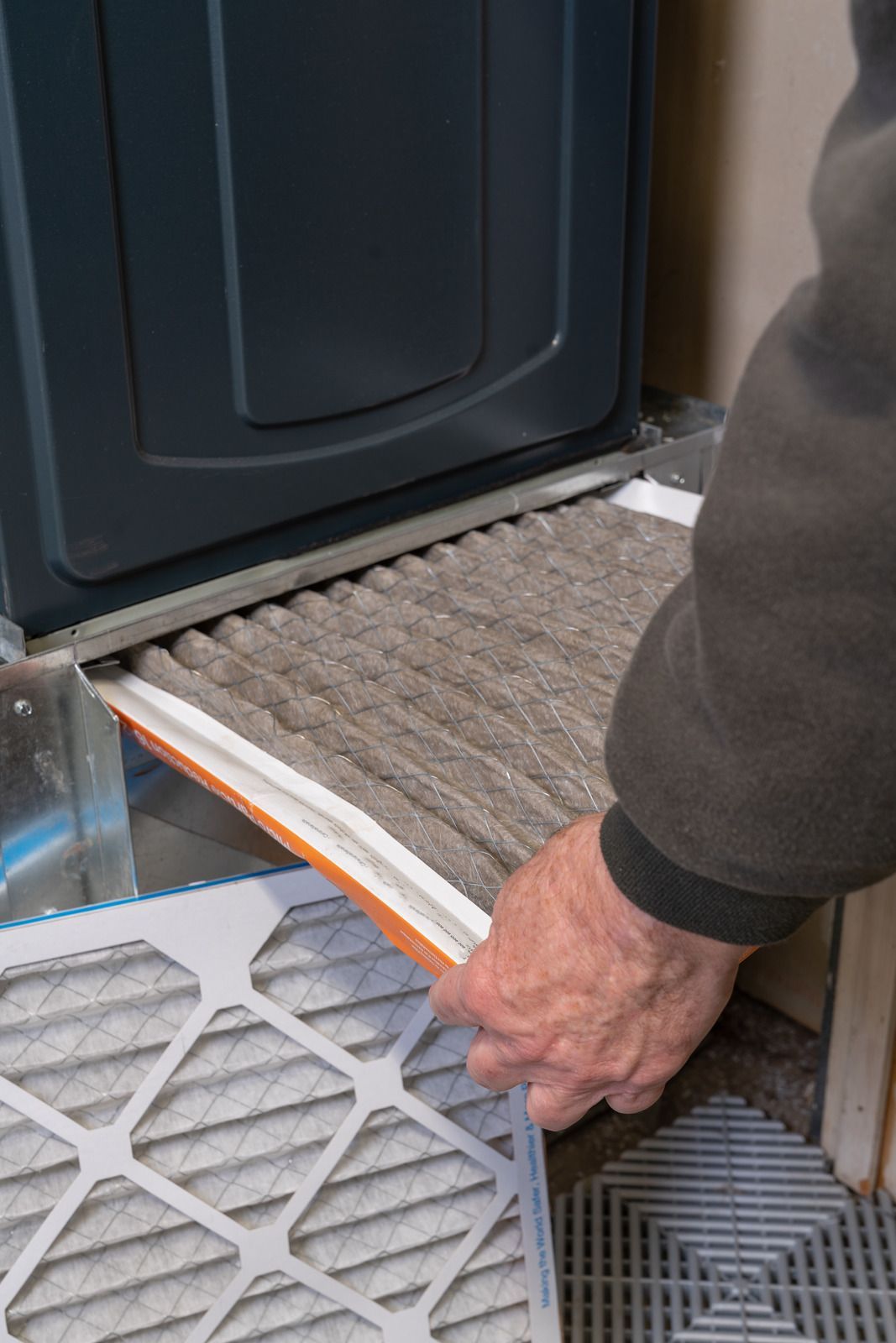 Person replacing a dirty air filter in a furnace. Gray filter filled with dust, orange frame.