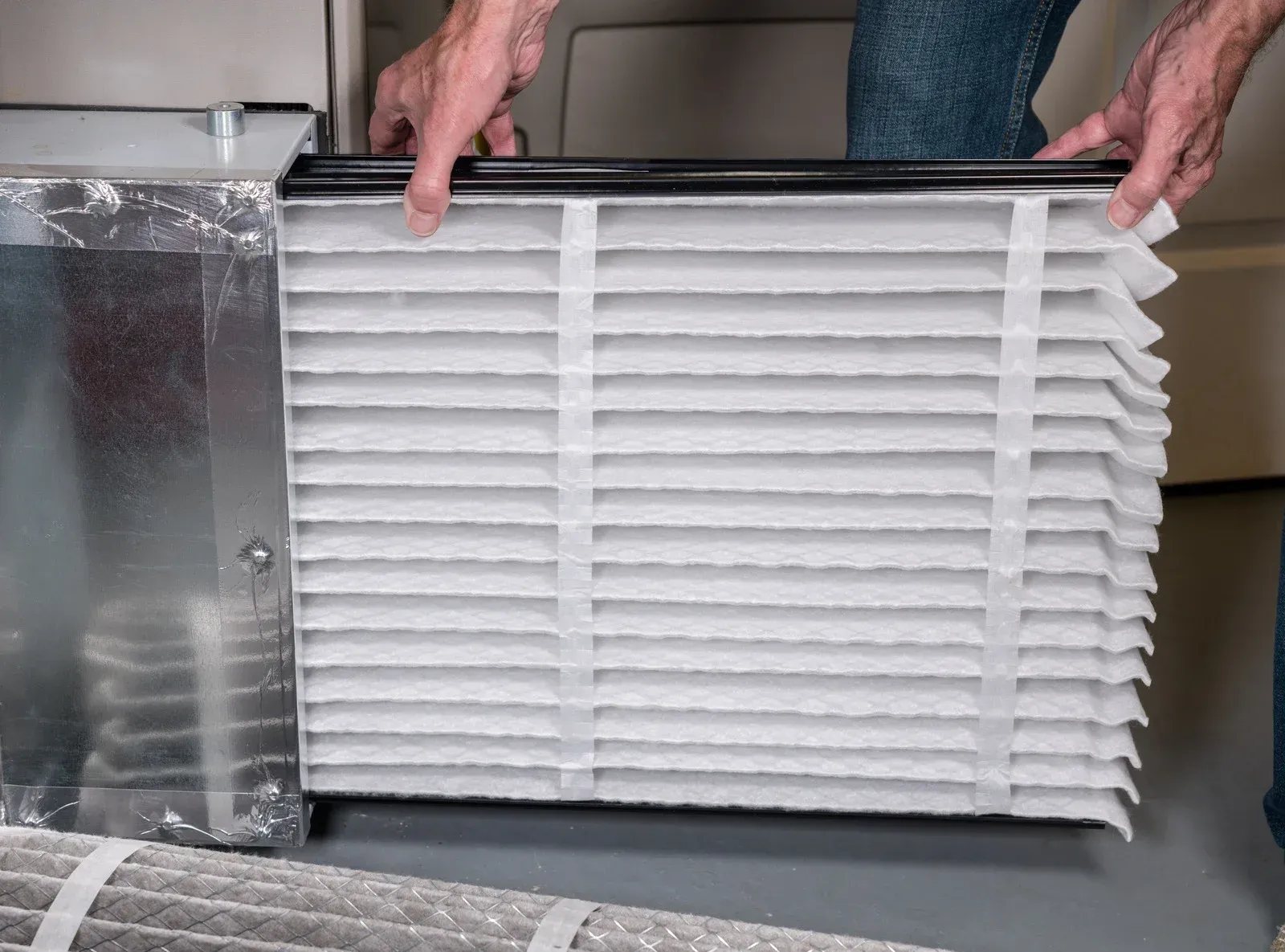 Person changing HVAC air filter. Hands holding a new, pleated filter.