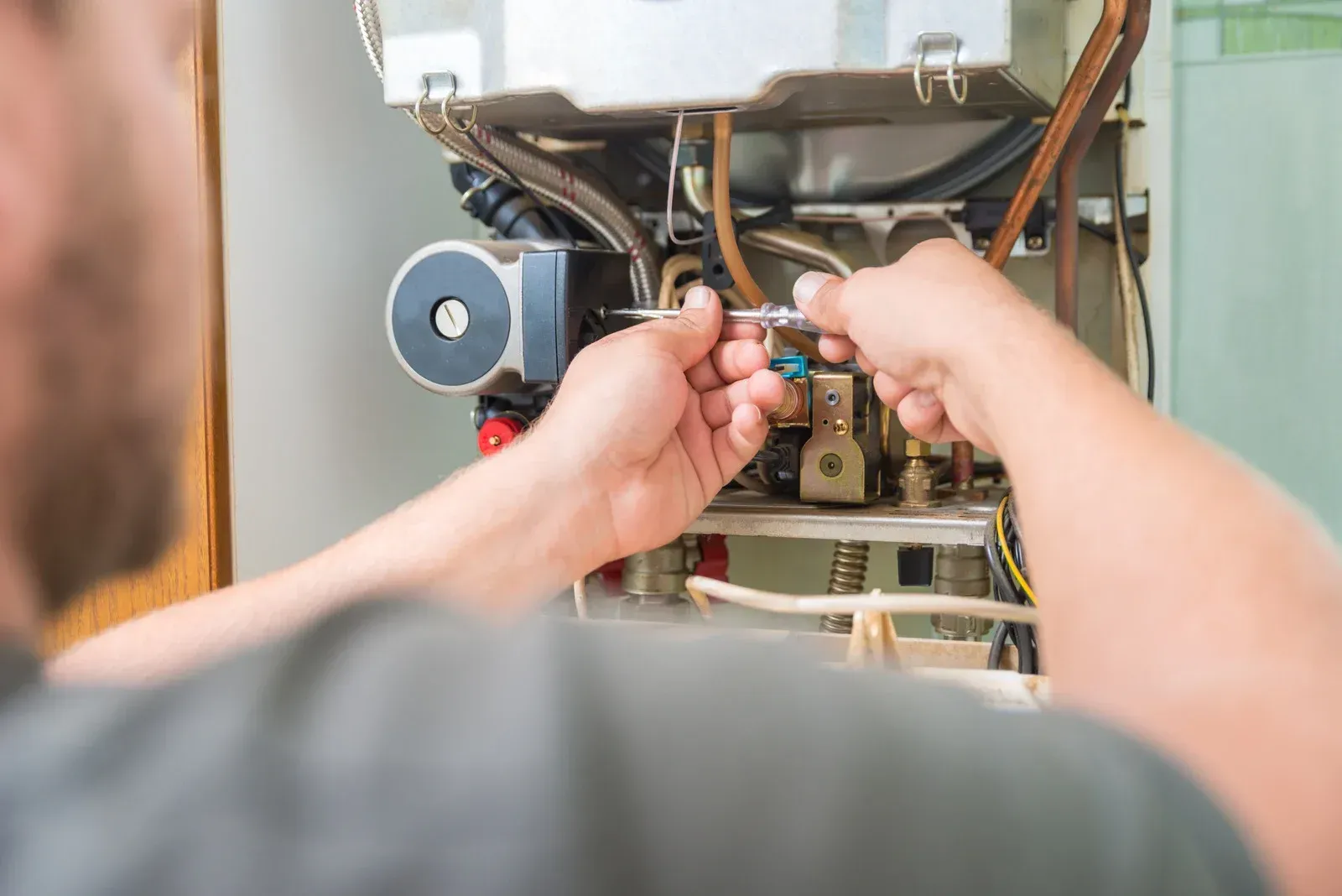 A person repairs a boiler with a wrench, working on the internal components.