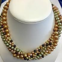 Multi-strand pearl necklace, varying shades of brown, green and black, on a white bust.