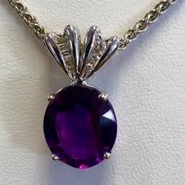Silver necklace pendant with a large, oval-cut, purple gemstone and small accent diamonds.