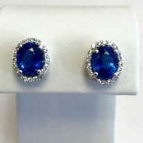 Sapphire stud earrings with diamond halos displayed on a white stand.
