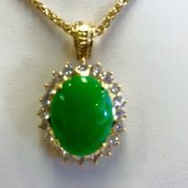 Gold necklace with a vibrant green gemstone pendant encircled by clear stones.
