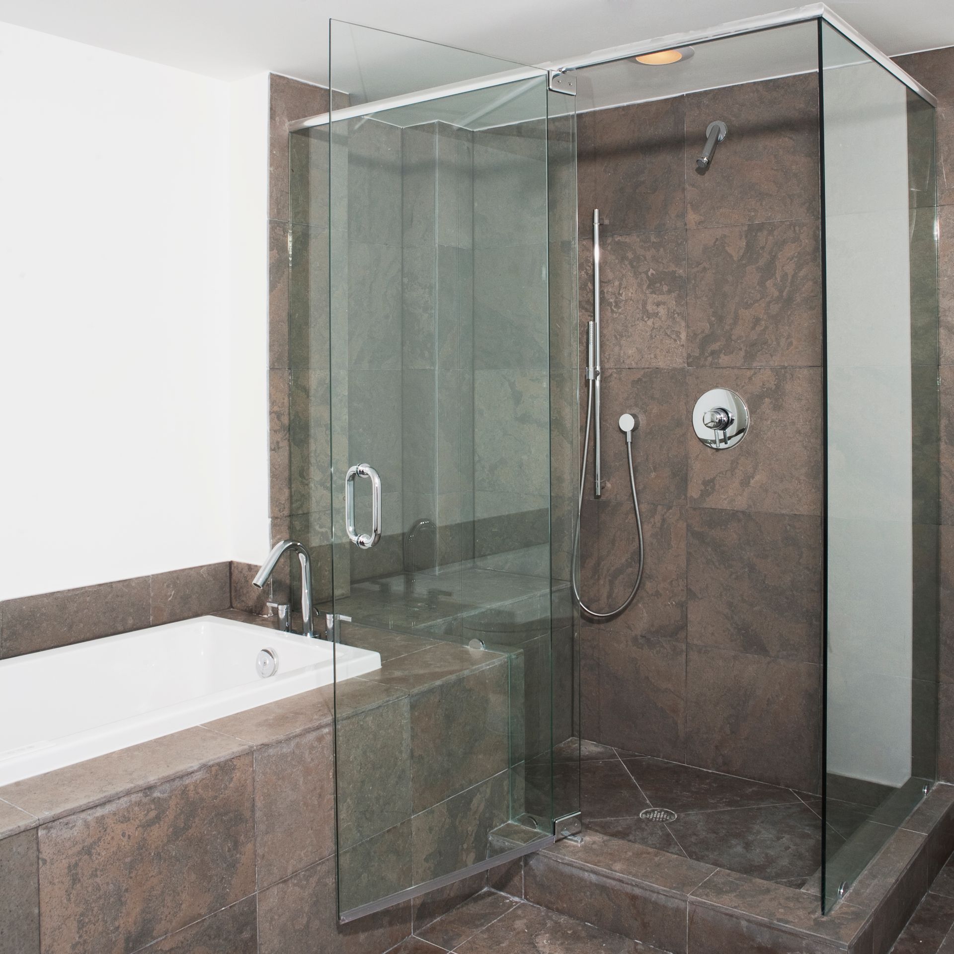 Modern bathroom with glass shower enclosure and built-in bathtub with stone tiles.