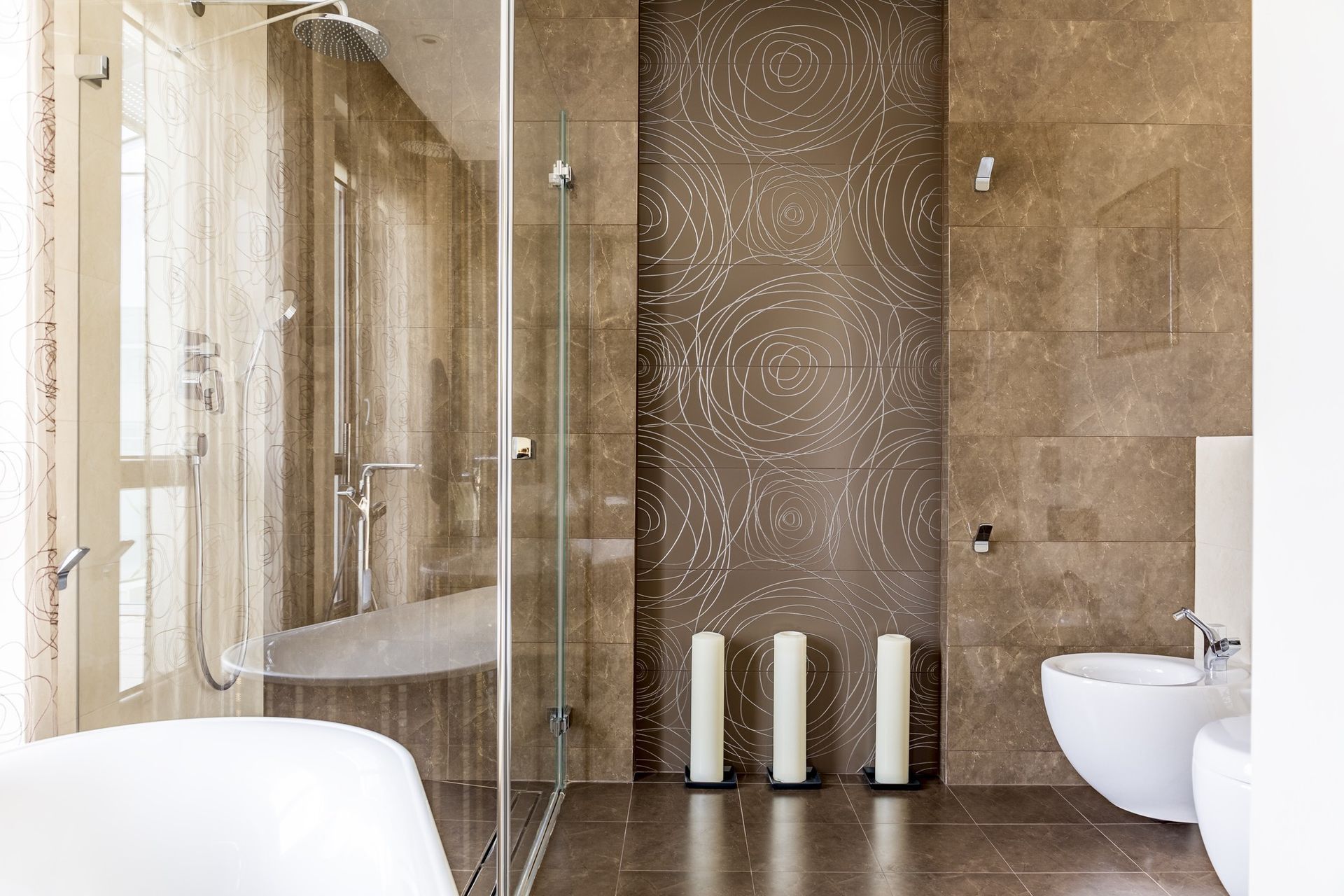 Glass shower enclosure in a bathroom with brown decorative tiles and abstract patterns and candles.