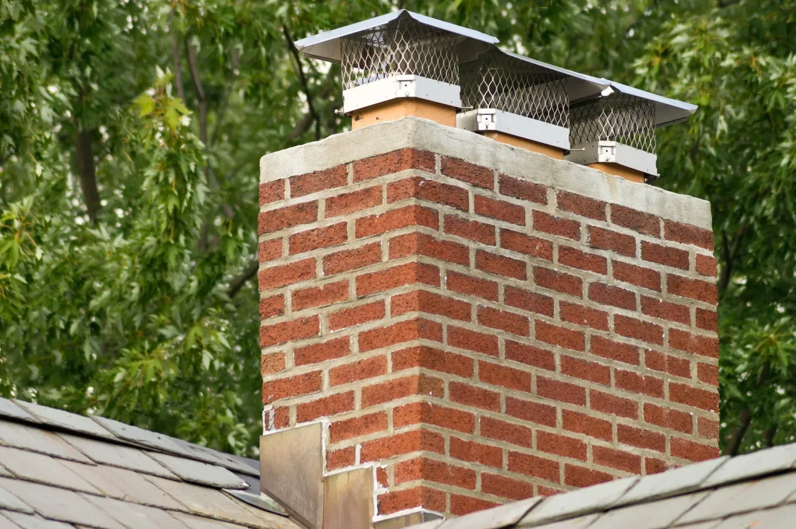 A brick chimney on top of a roof with trees in the background