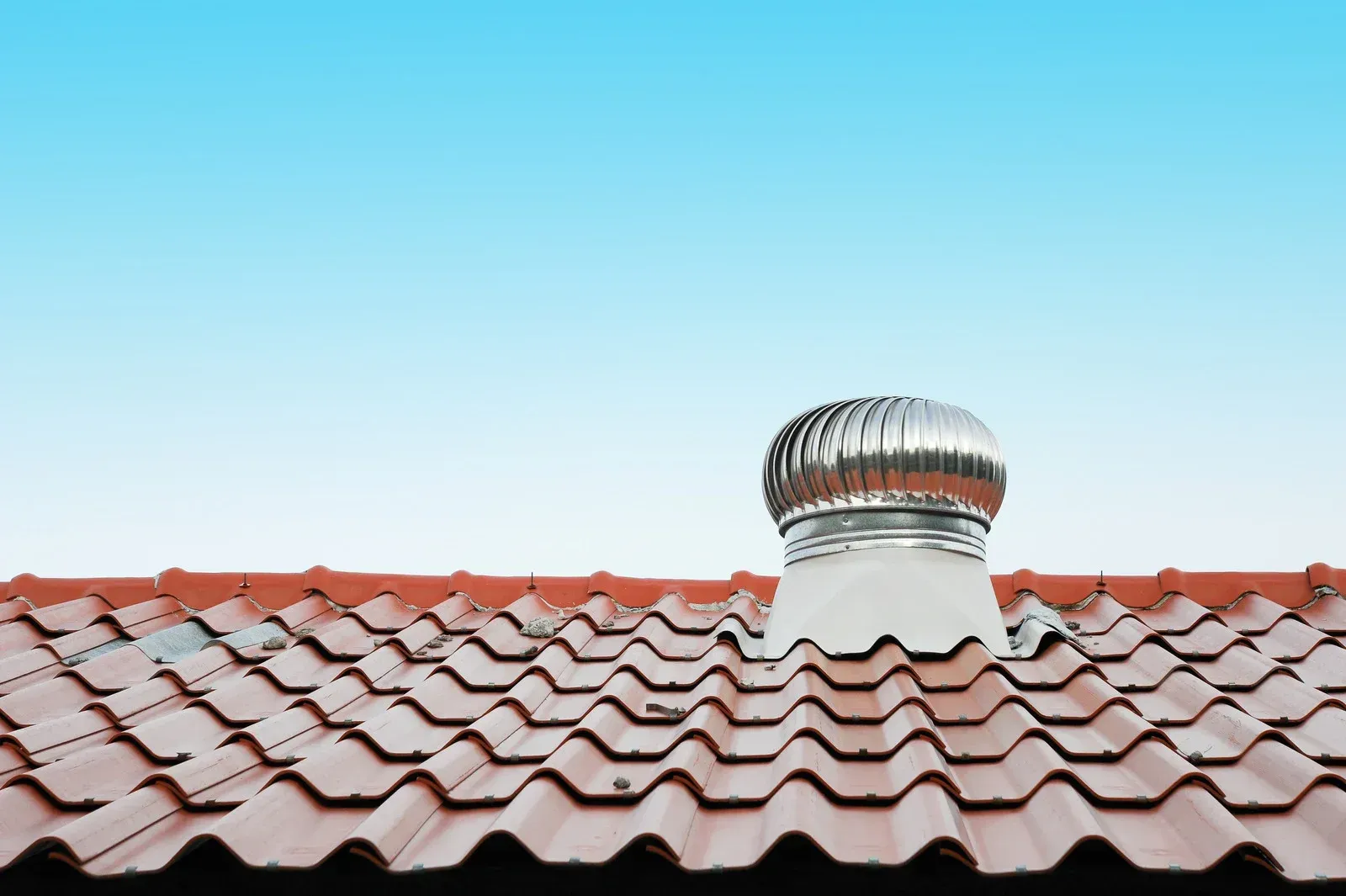 A roof with a fan on top of it and a blue sky in the background.