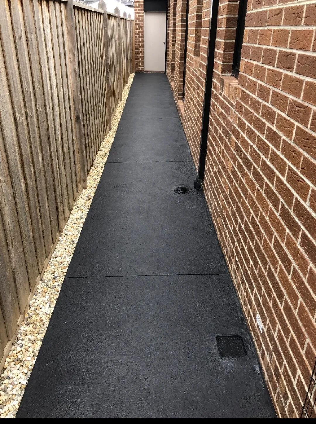 A black walkway between two brick buildings with a wooden fence.