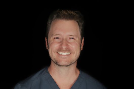 Woman with blonde hair wearing a black turtleneck speaks. Background includes costumed figures.