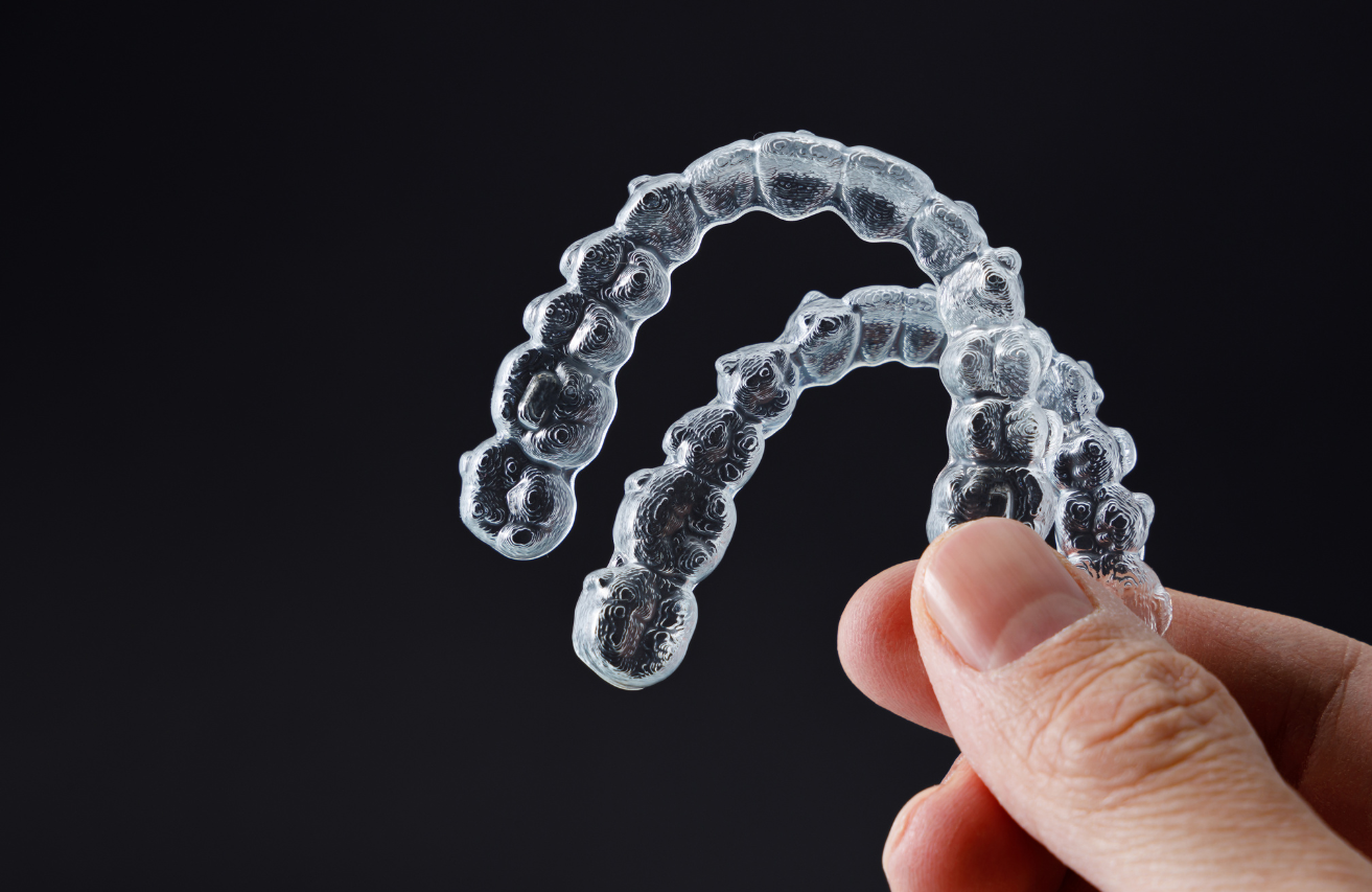 Hand holding a pair of clear aligner trays against a dark background.