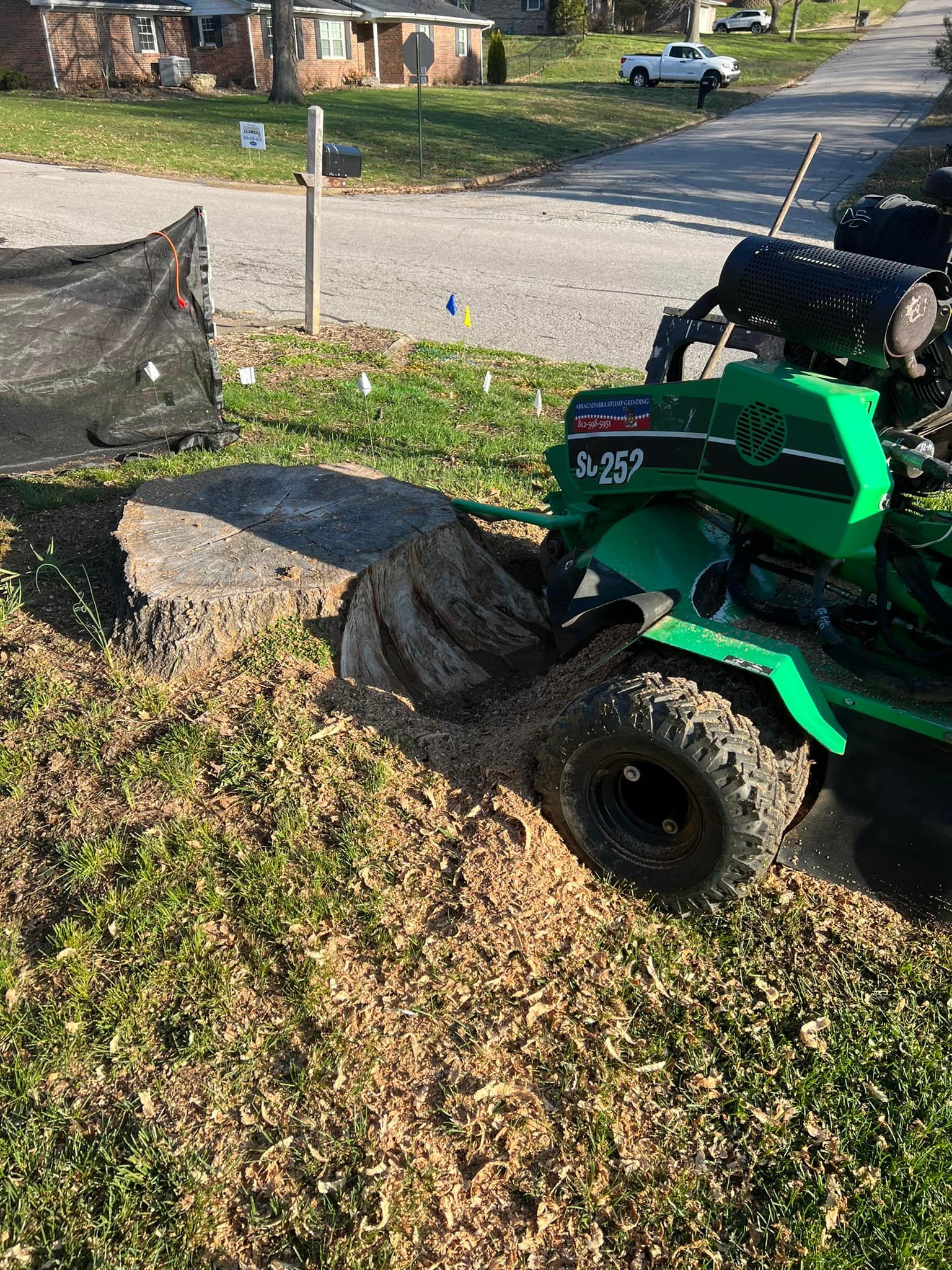 A green tractor is stump grinding a tree stump in a yard