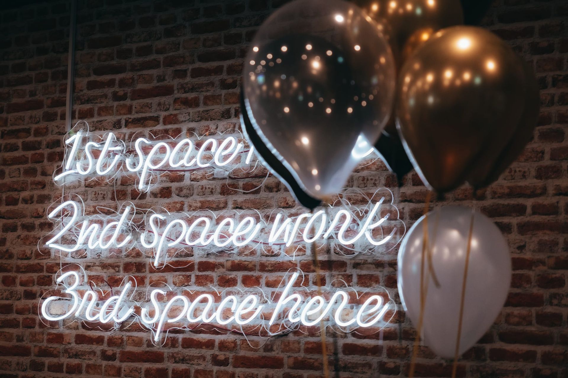 A brick wall with balloons and a neon sign that says 1st space 2nd space work 3rd space here