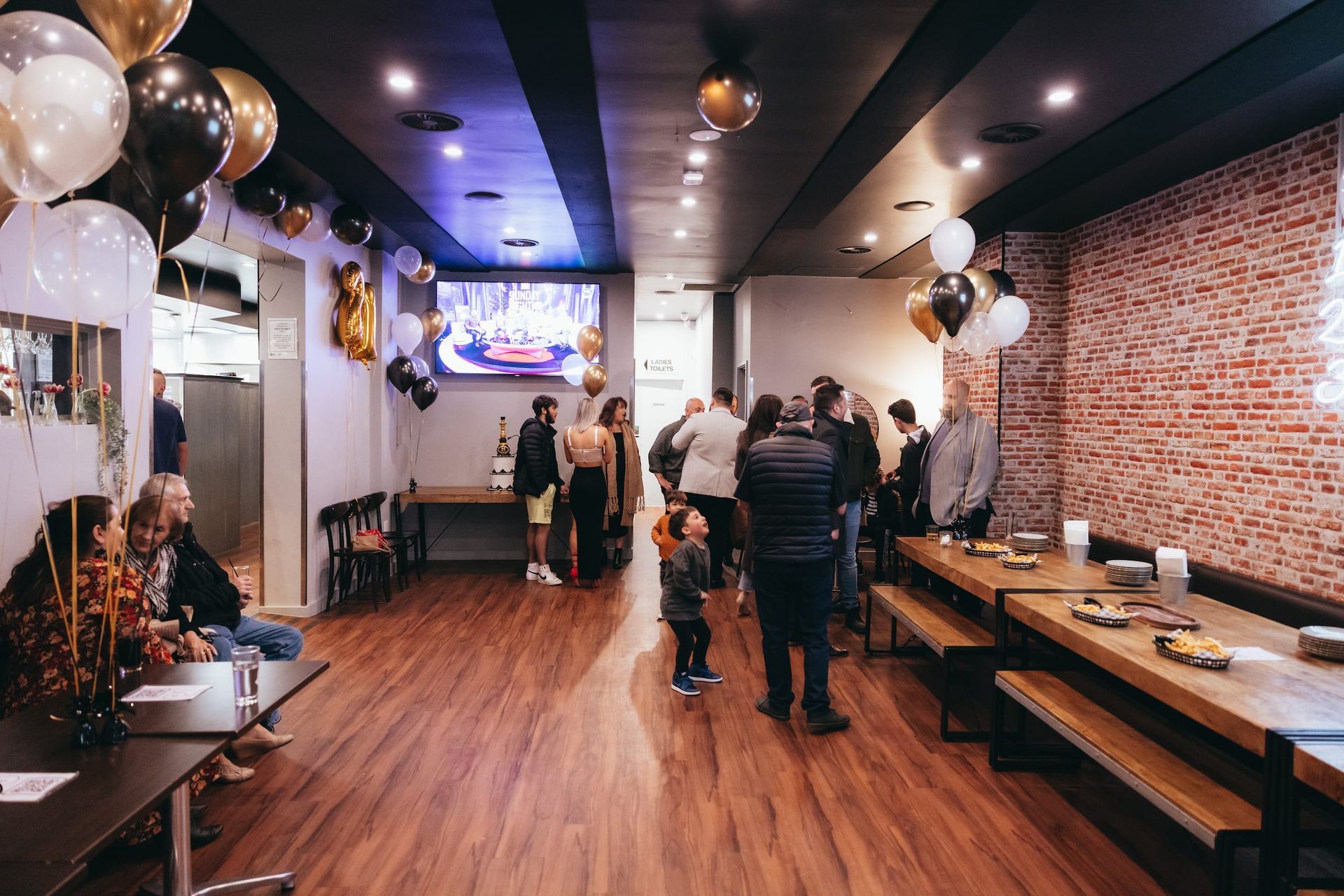 A group of people are standing in a room filled with tables and balloons.