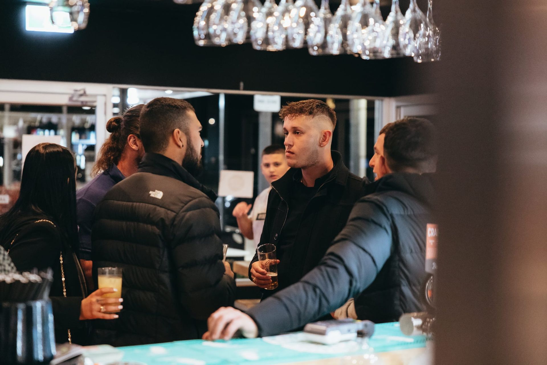 A group of people are standing around a bar talking to each other.