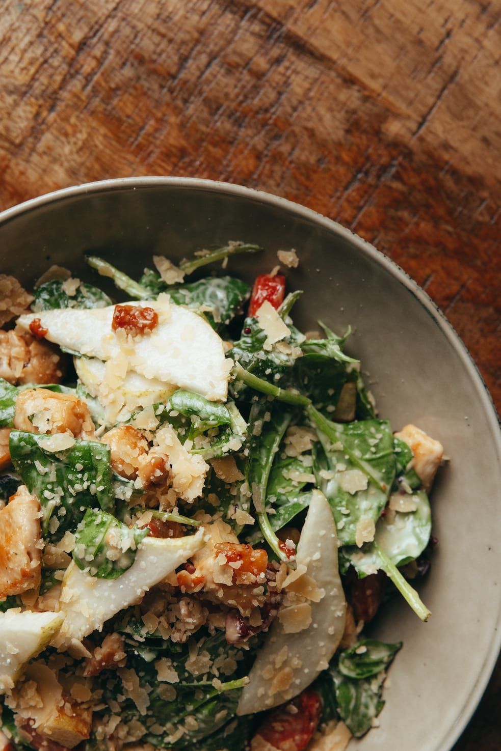 A close up of a salad in a bowl on a wooden table.