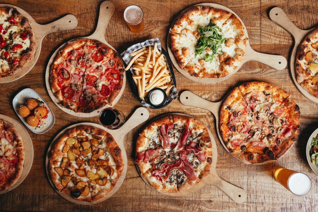 A wooden table topped with a variety of pizzas and french fries.