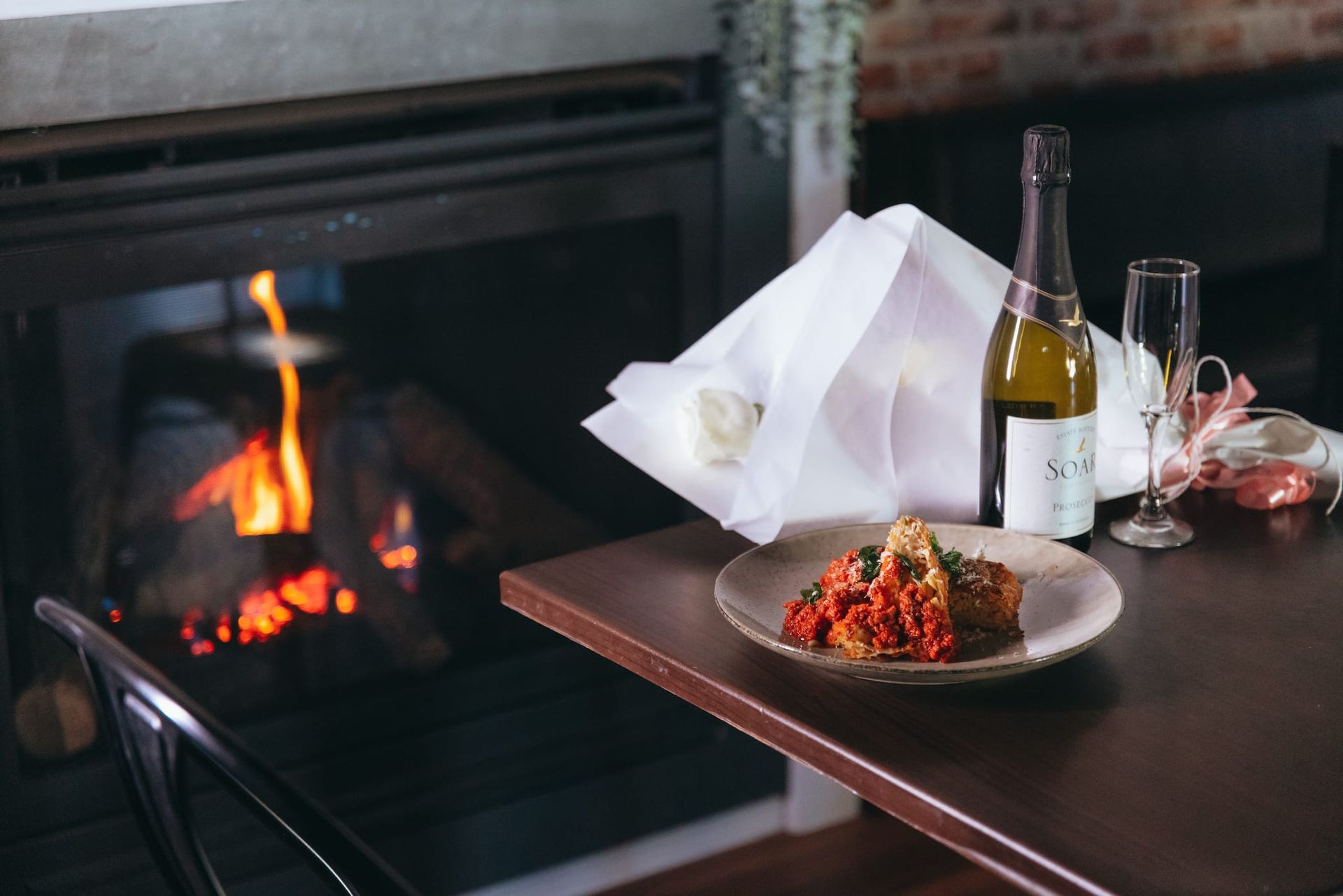 A plate of food and a bottle of wine on a table in front of a fireplace.