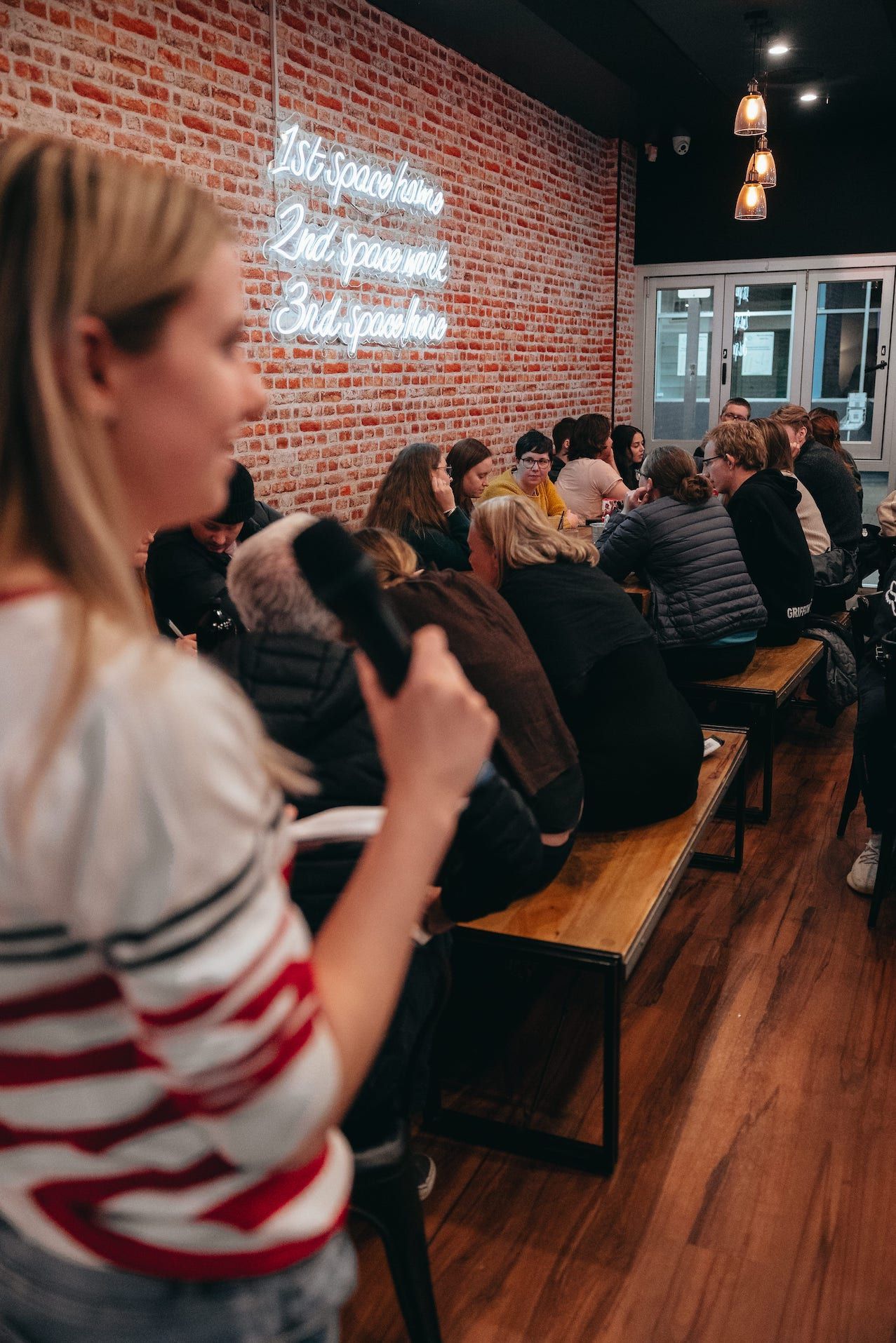 A woman is holding a microphone in front of a crowd of people sitting on benches.