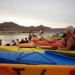 A group of people are sitting in kayaks on a lake.