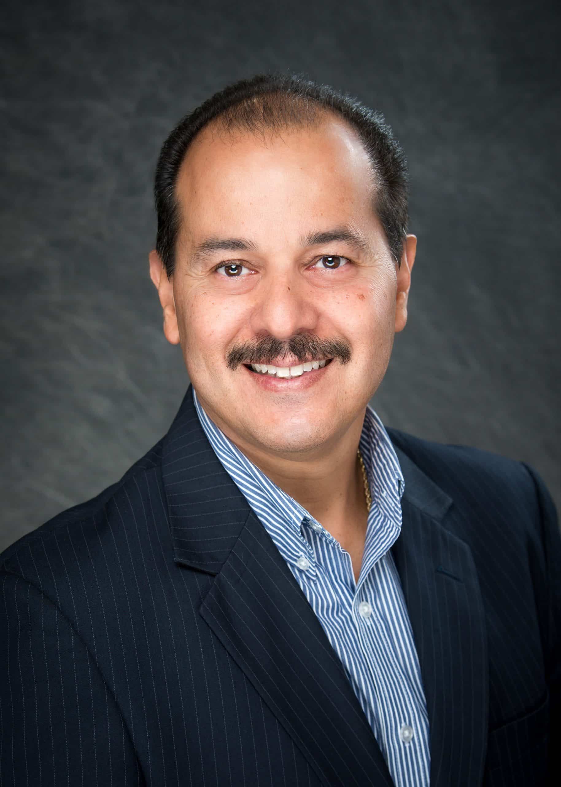 A man with a mustache is wearing a suit and smiling for the camera.