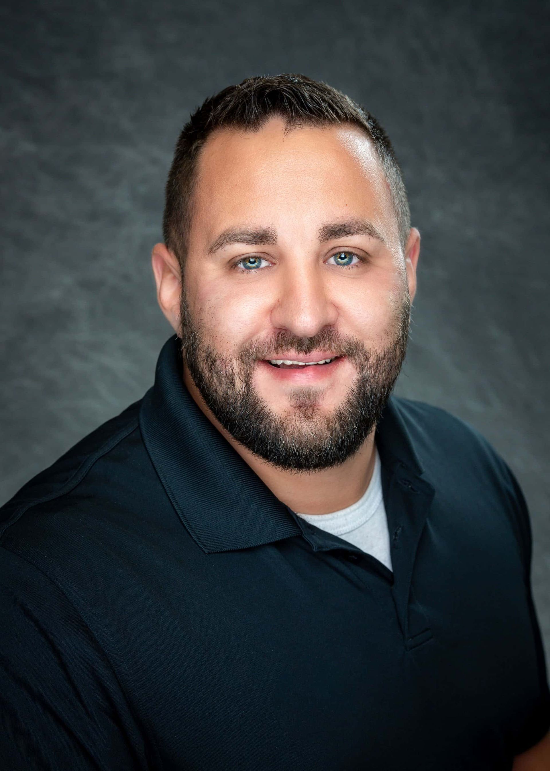 A man with a beard is wearing a blue shirt and smiling for the camera.