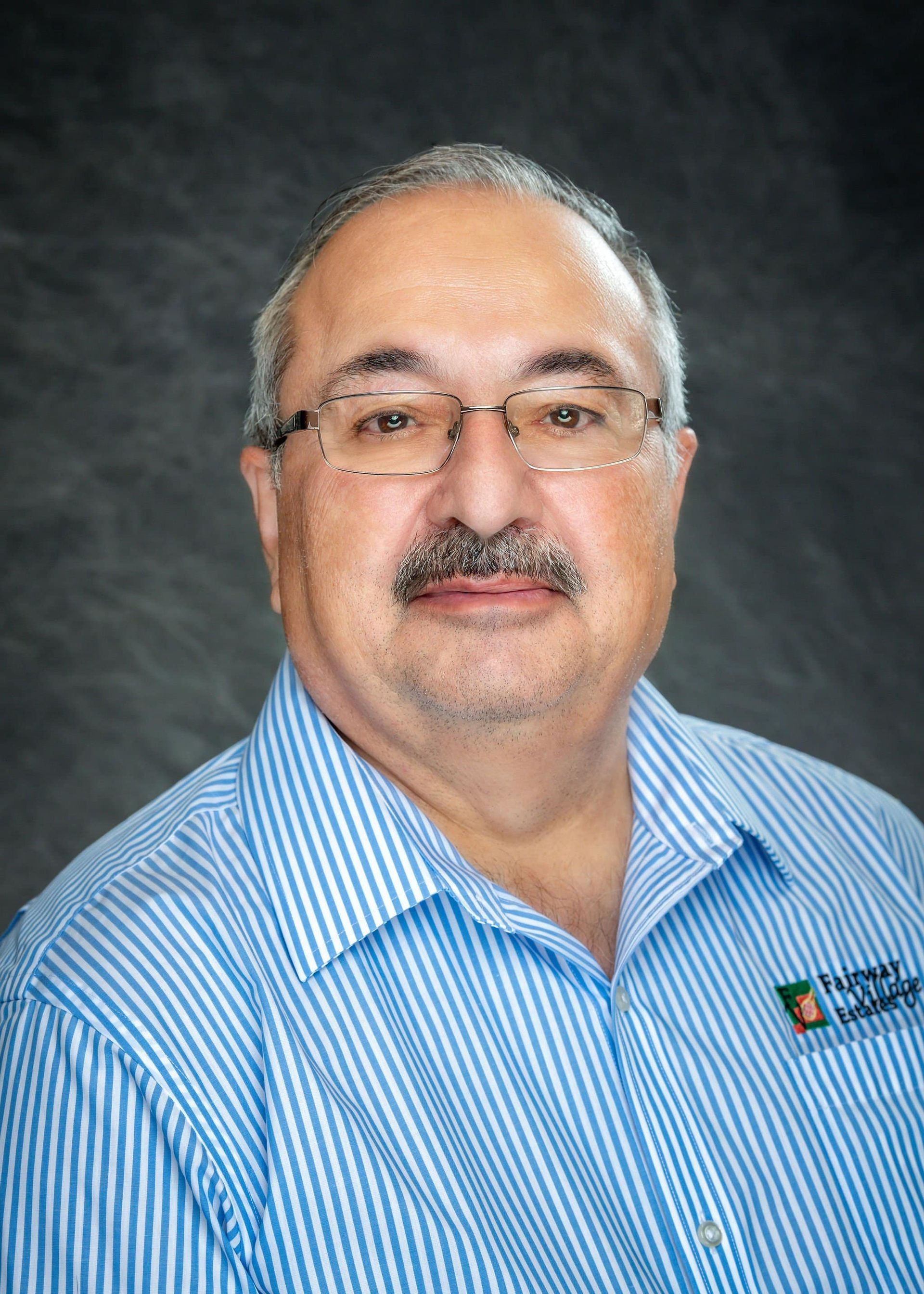 A man with glasses and a mustache is wearing a blue and white striped shirt.