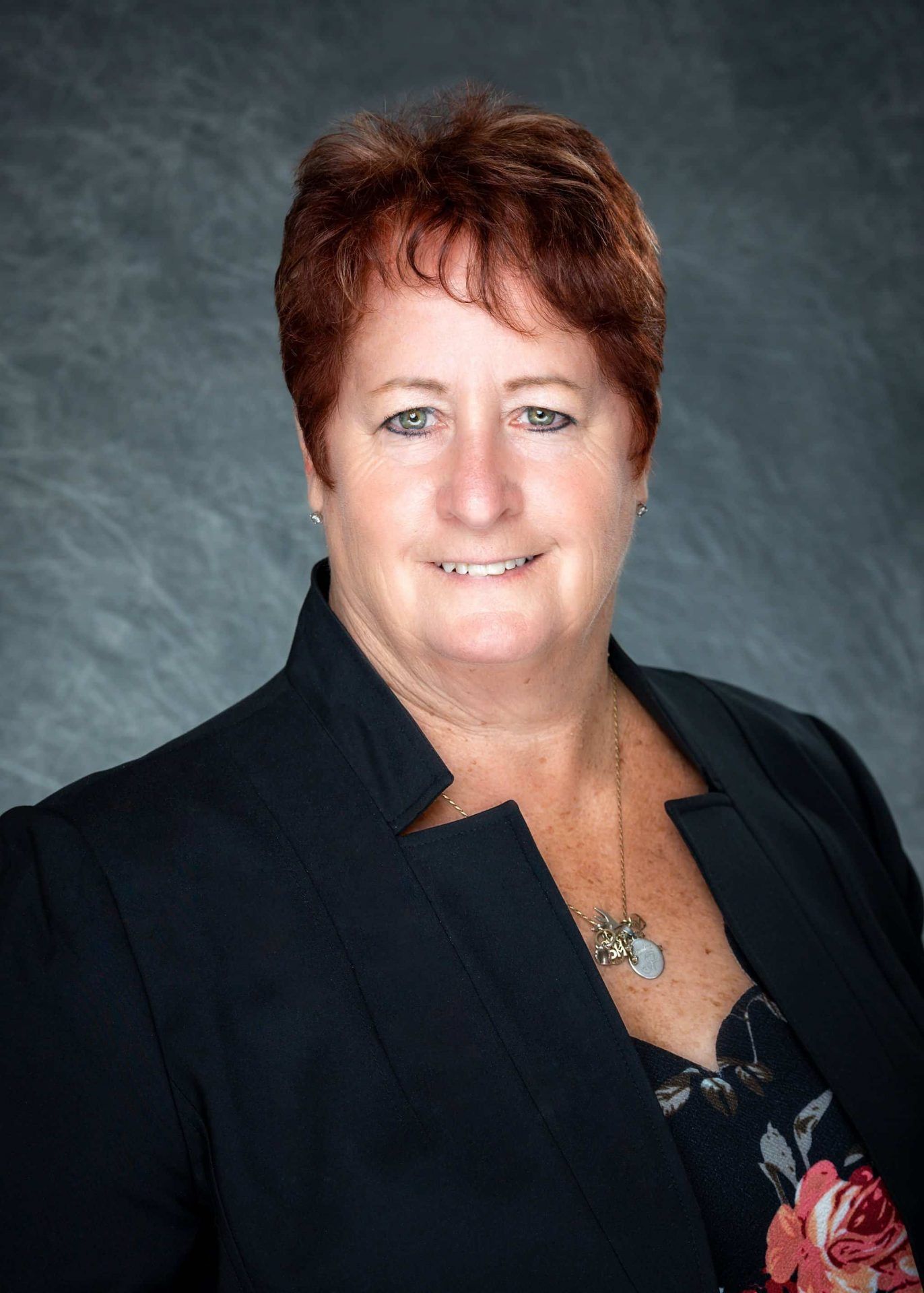 A woman with red hair is wearing a black jacket and a necklace.