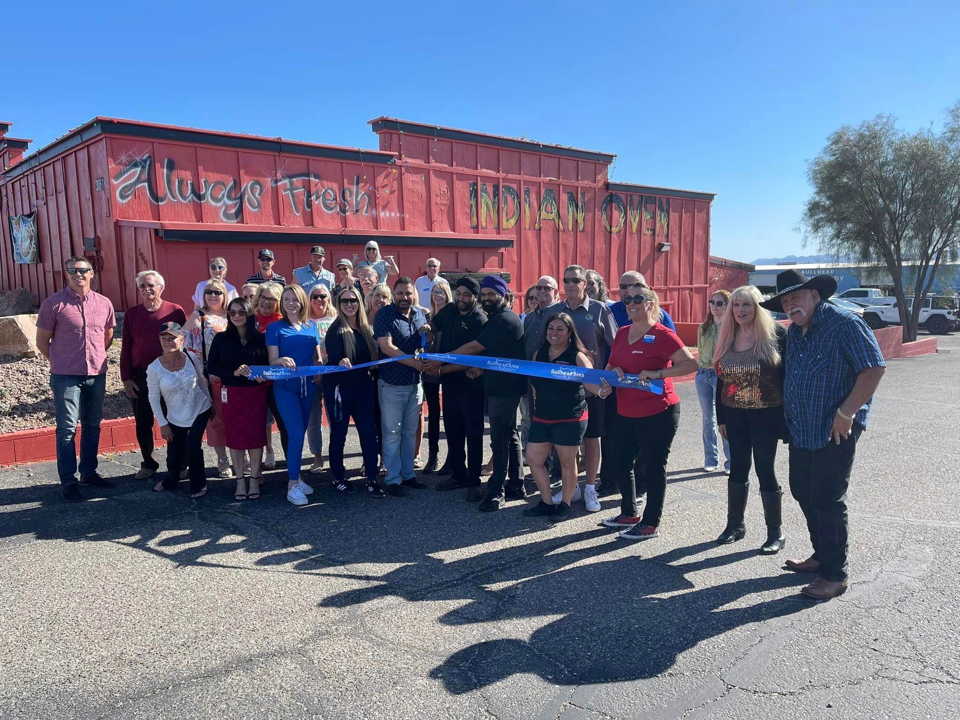 A group of people are standing in front of a building holding a blue ribbon.
