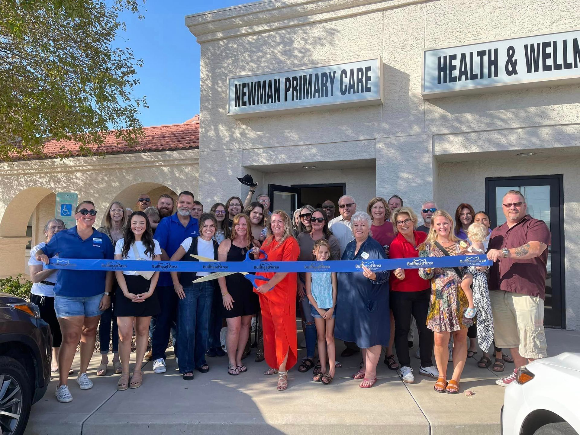 A large group of people are standing in front of a building holding a blue ribbon.