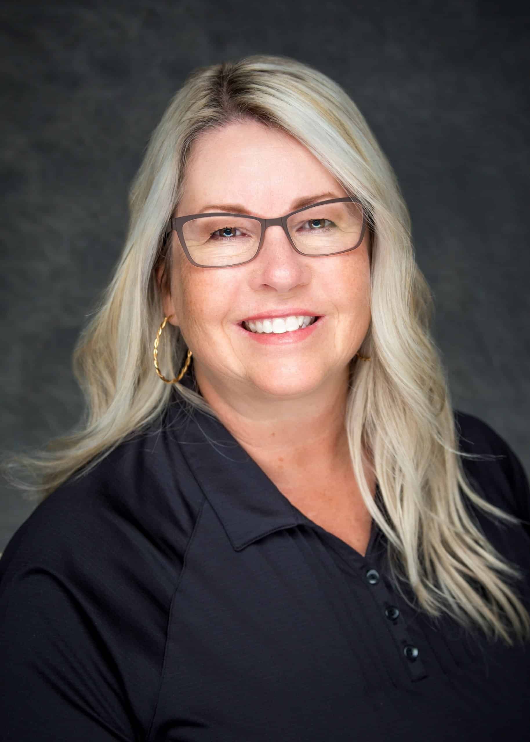 A woman wearing glasses and a black shirt is smiling for the camera.