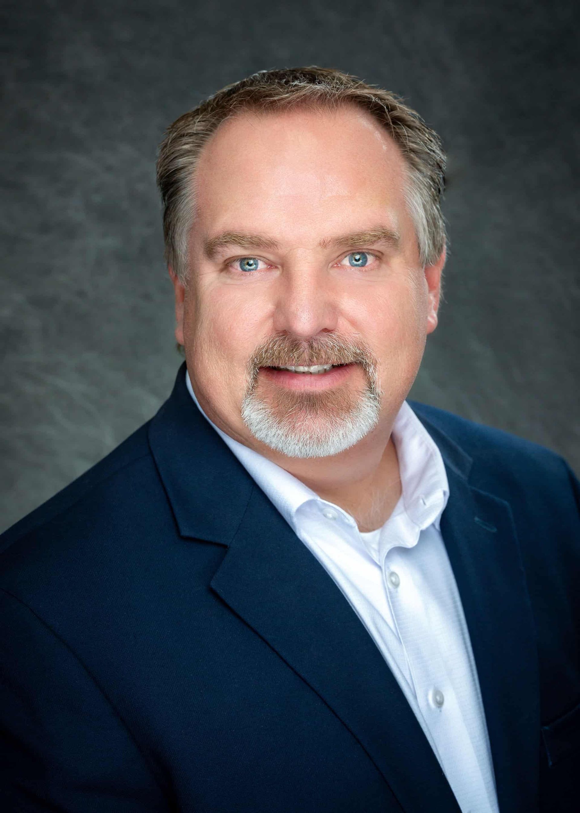 A man with a beard is wearing a blue suit and white shirt.