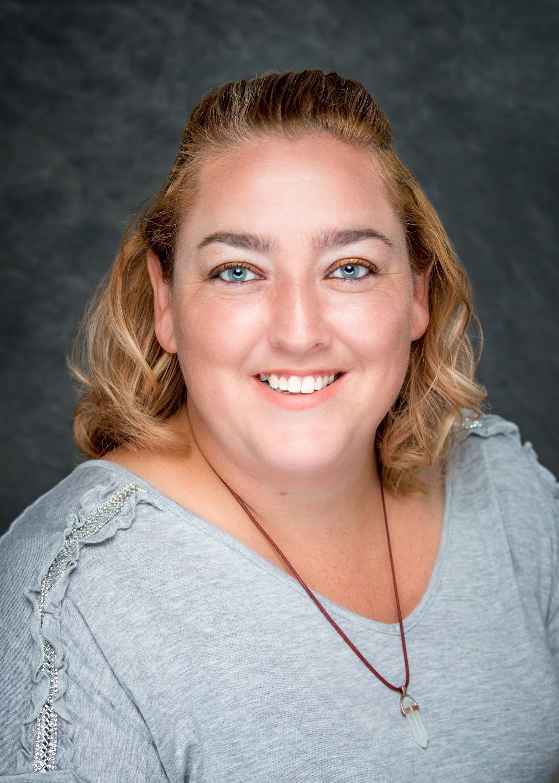 A woman wearing a gray shirt and a red necklace is smiling for the camera.