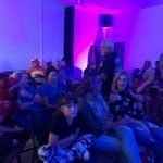 A group of people are sitting in a room with purple lights.