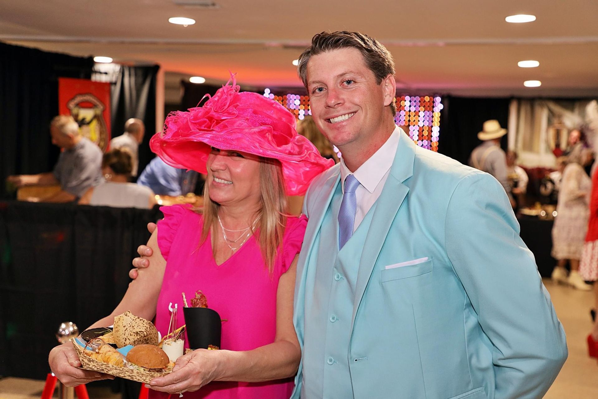 A woman in a pink hat is standing next to a man in a blue suit.