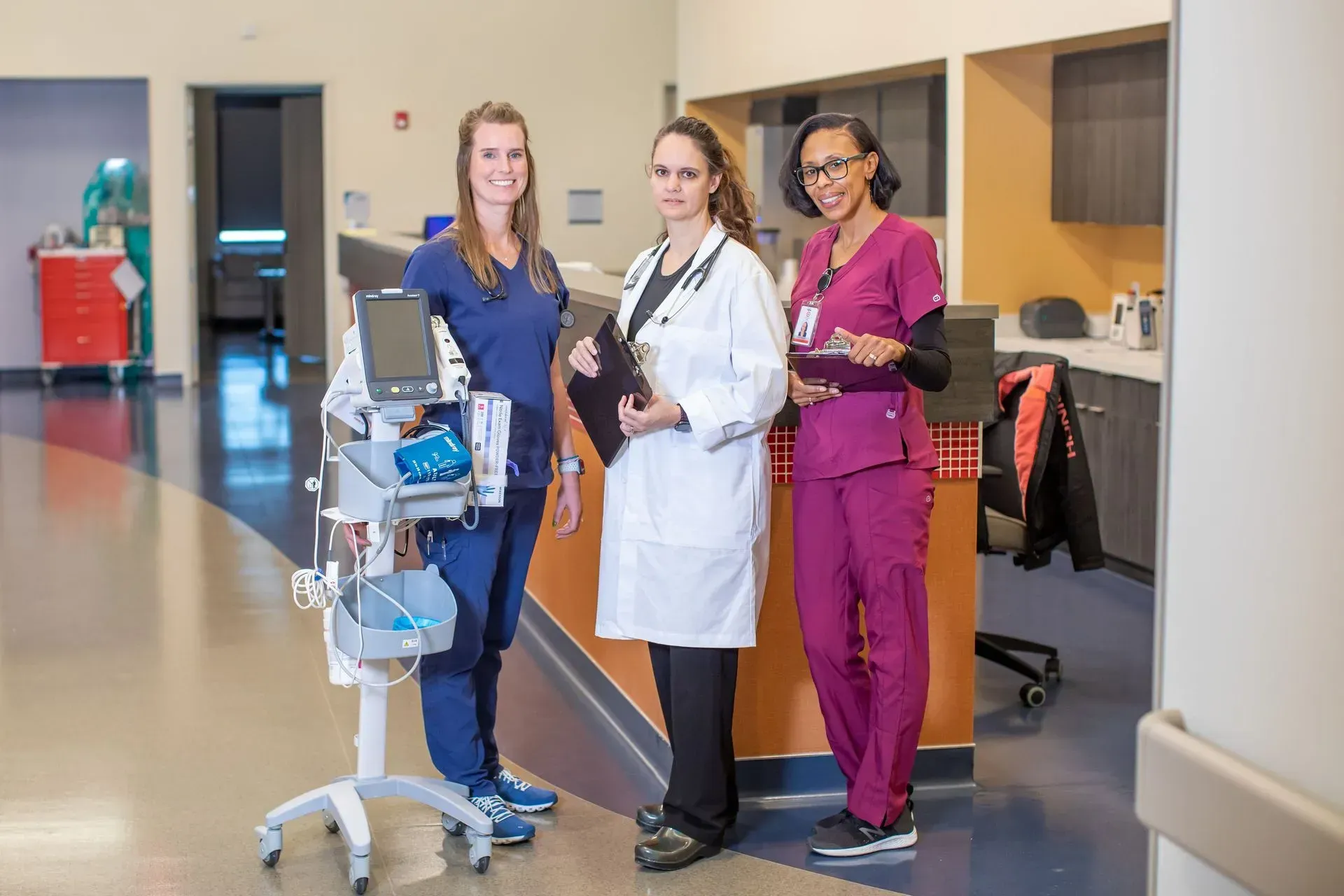 Three nurses and a doctor are standing next to each other in a hospital hallway.