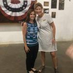 Two women are posing for a picture in front of an american flag.