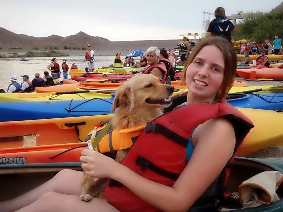 A woman is holding a dog in front of a row of kayaks