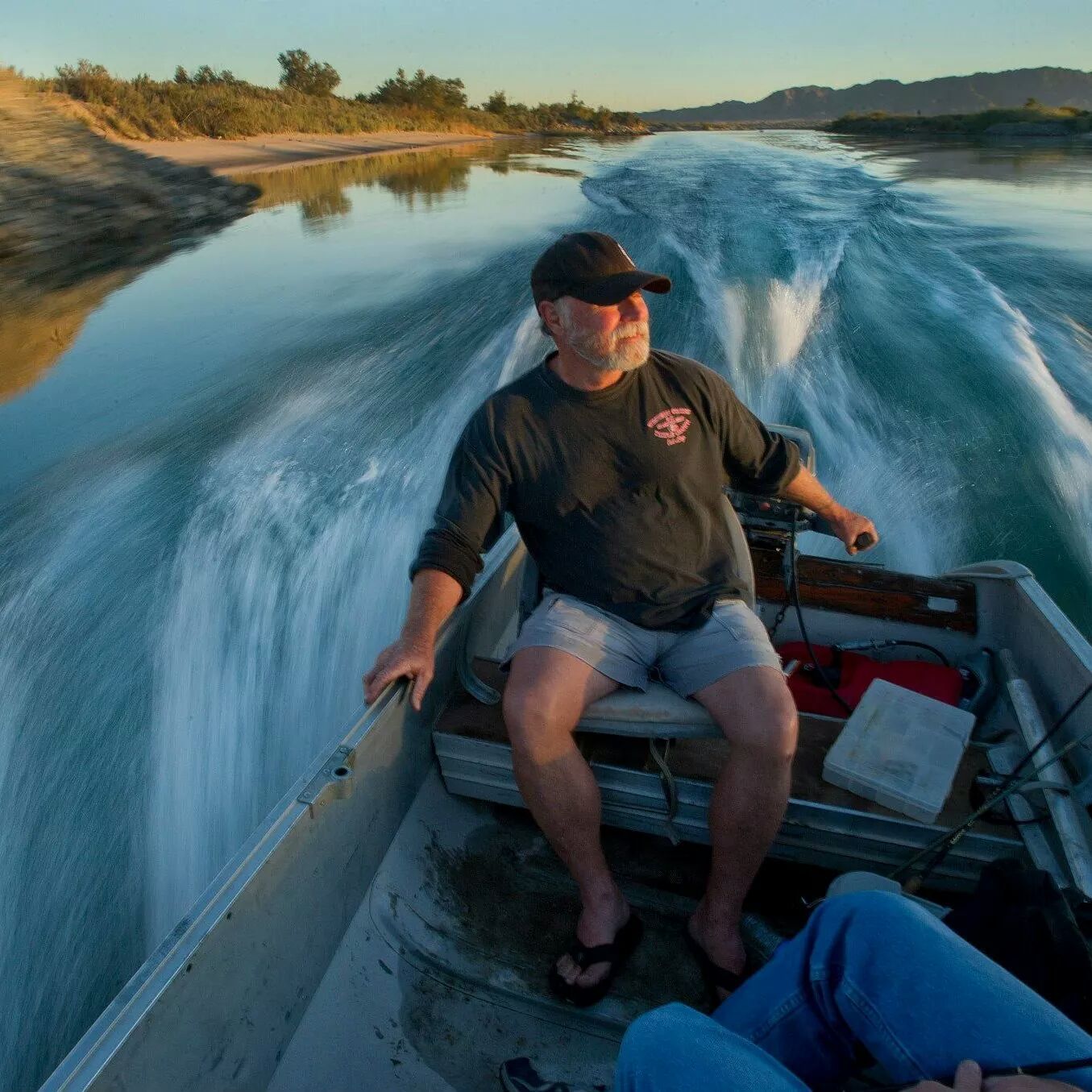 A man in a black shirt is sitting in a boat on a river