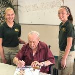 A man in a wheelchair is sitting at a table with two girls standing behind him.