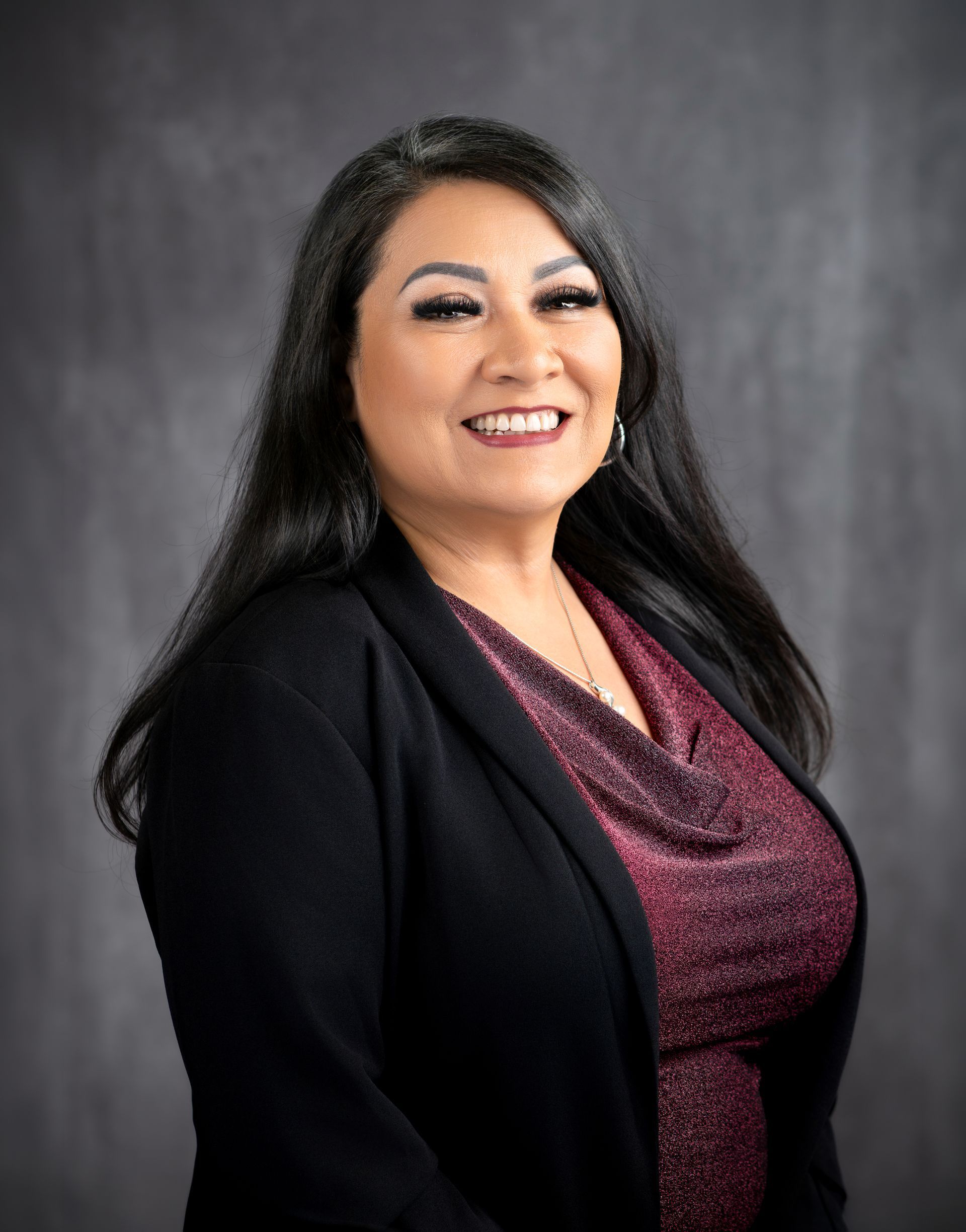 A woman wearing a white shirt and a black jacket is smiling for the camera.