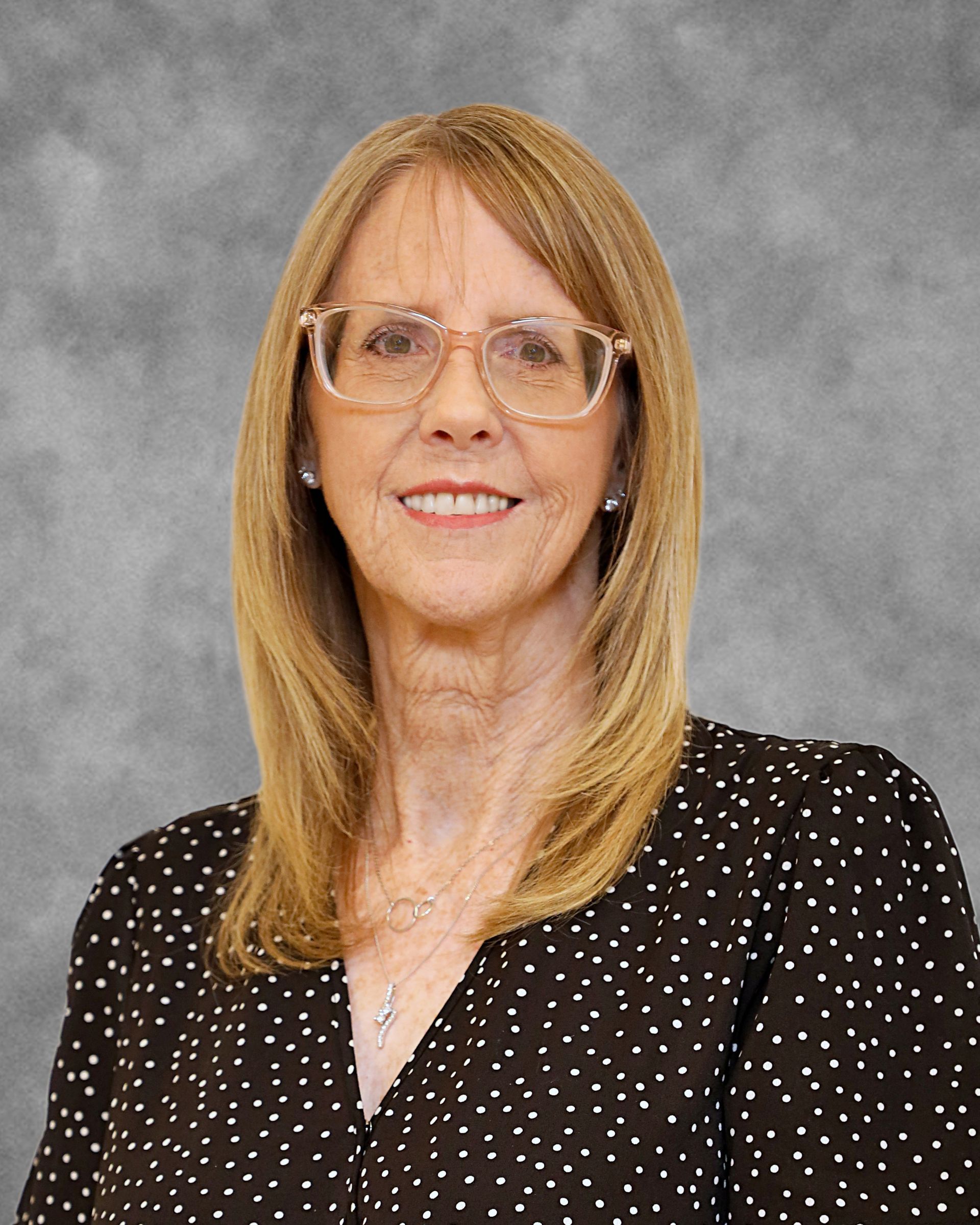 A woman wearing glasses and a black polka dot shirt is smiling for the camera.