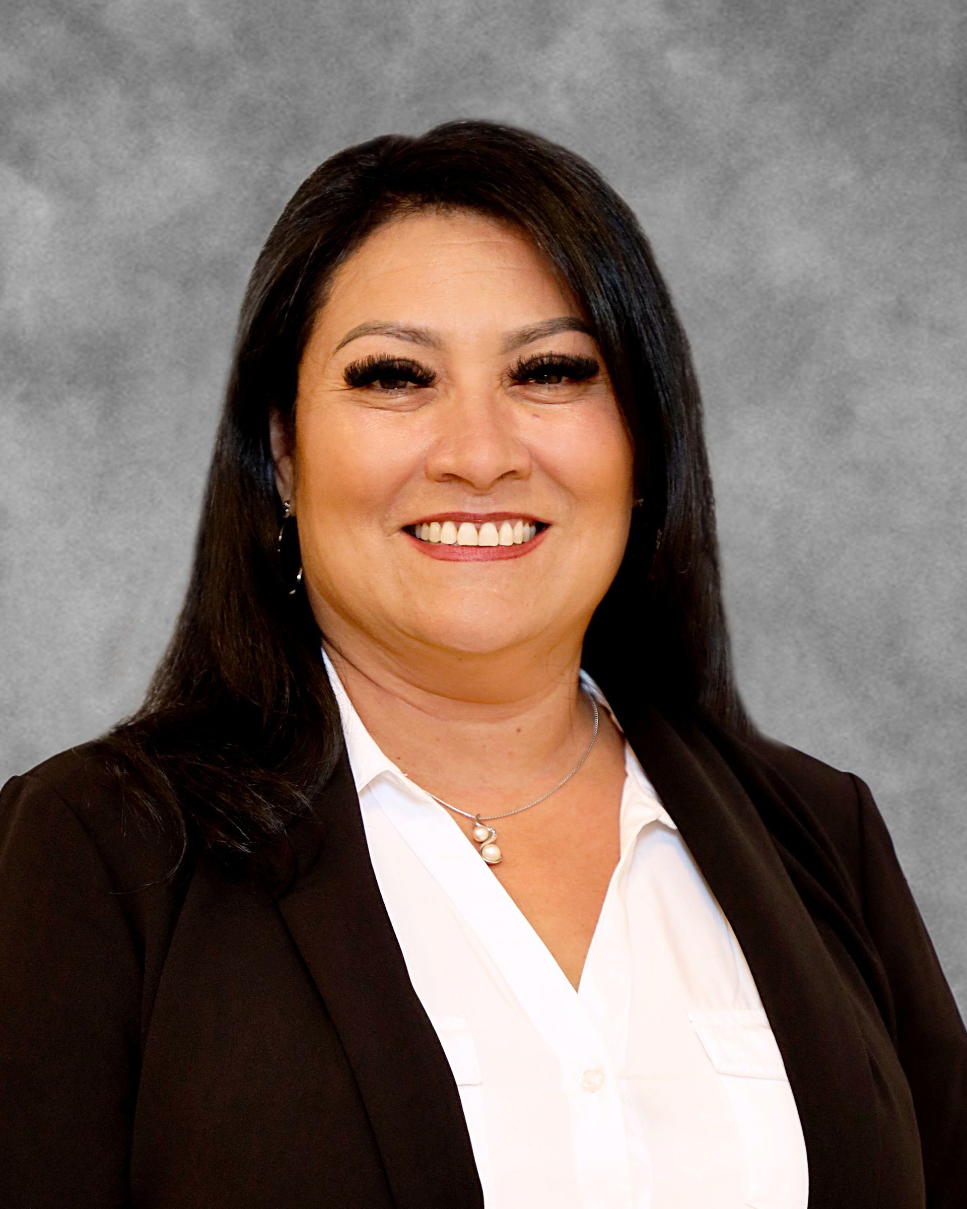 A woman wearing a white shirt and a black jacket is smiling for the camera.