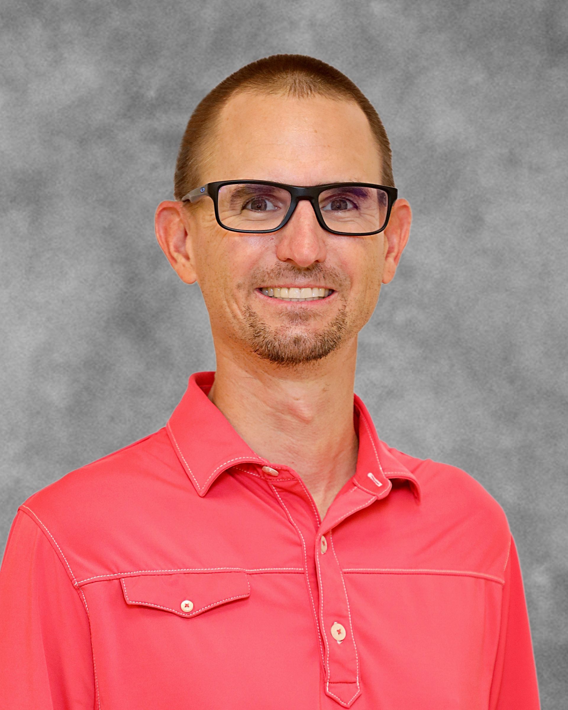 A man wearing glasses and a red shirt is smiling for the camera.