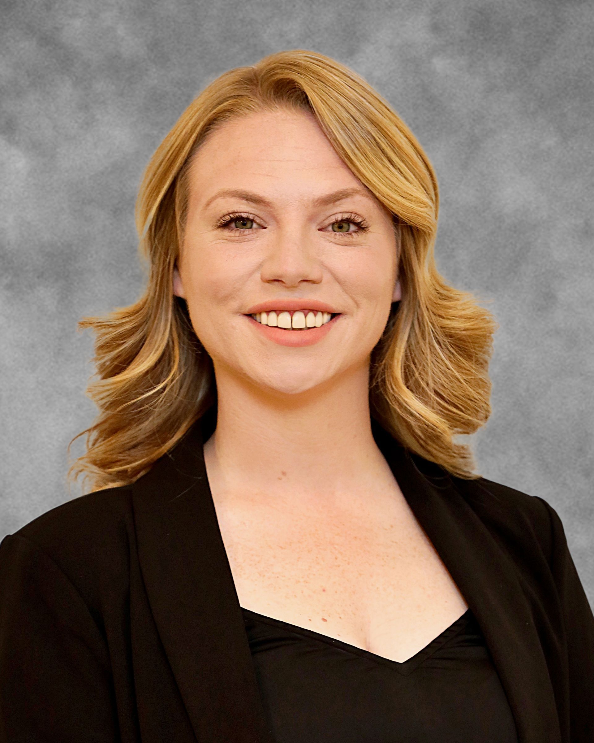 A woman with blonde hair is smiling and wearing a black jacket