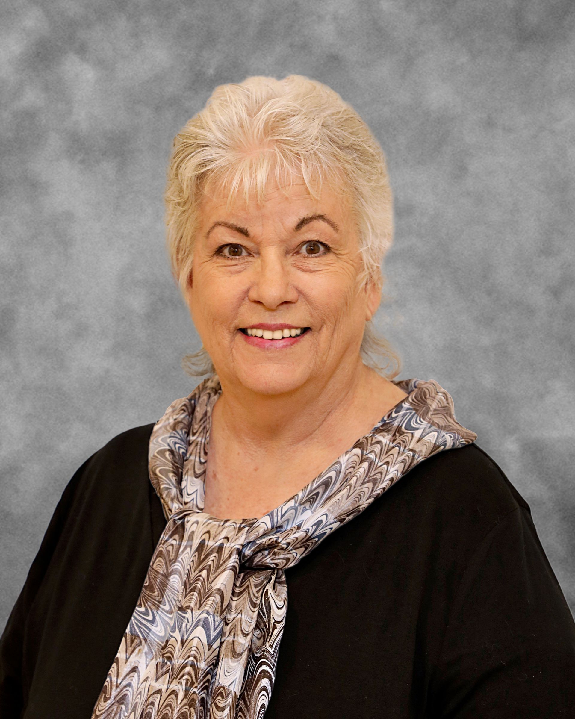 A woman wearing a scarf and a black jacket is smiling for the camera.