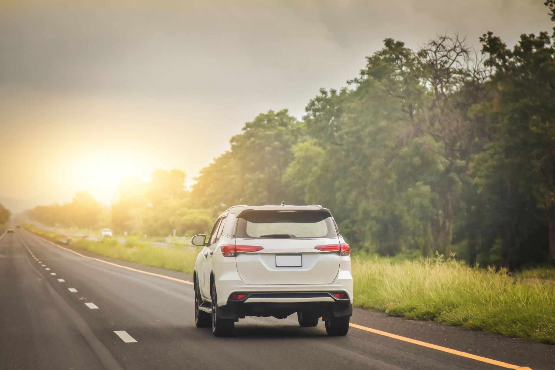 A white suv is driving down a highway at sunset.