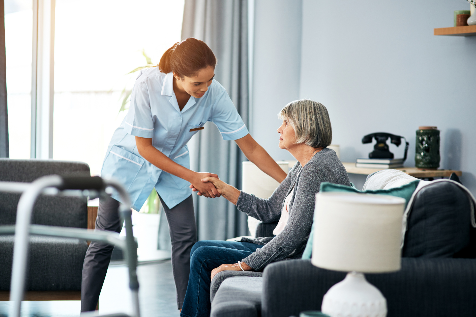 A nurse is shaking hands with an elderly woman in a living room.