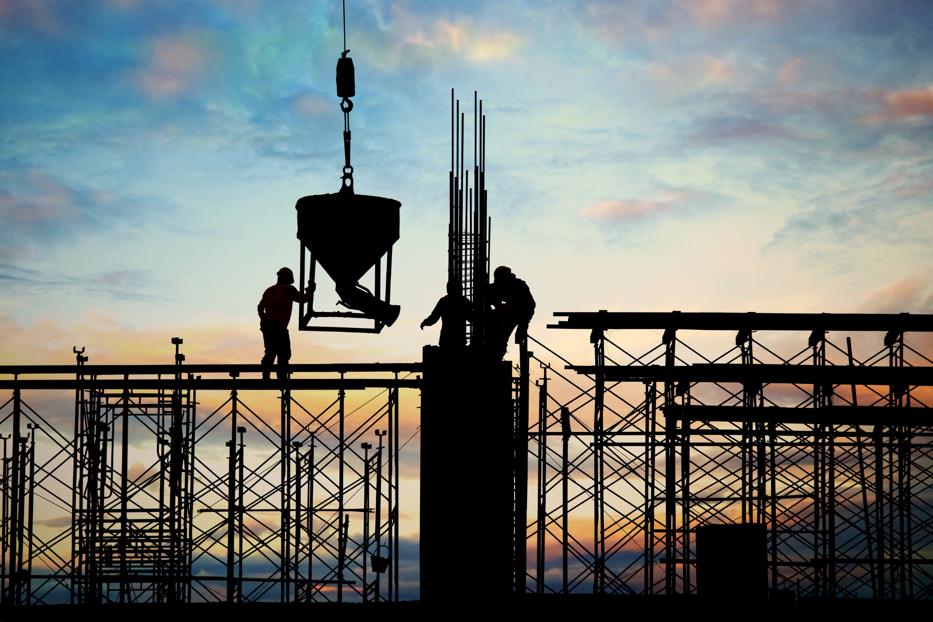 A group of construction workers are working on top of a building at sunset.